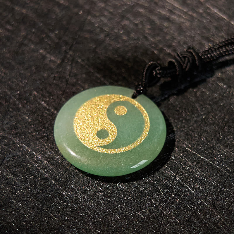 Yin Yang Crystal Necklace – Round green aventurine pendant with gold yin-yang engraving, smooth polished stone on black braid
