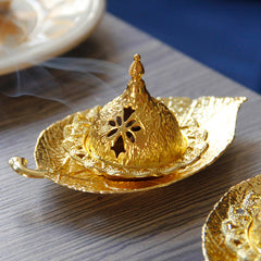Tibetan Gold Leaf Coaster Incense Burner – Gold burner with smoke rising from floral cutout dome on wood grain, metal incense holder