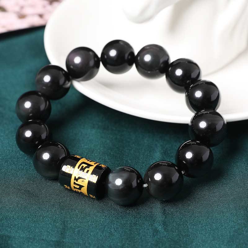 Rainbow Obsidian Bracelet – Side view of beaded bracelet with gold charm beside white ceramic dish, yoga jewelry