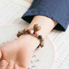 Bodhi Seed Lotus Mala – Worn on wrist with calligraphy book showing lotus charm, zen wrist mala