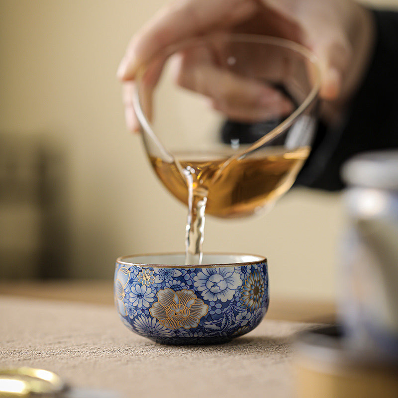 Lotus Chrysanthemum Ceramic Tea Cup - Amber tea pouring into blue-white cup, gongfu tea ritual
