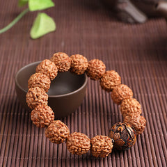 Rudraksha PiXiu Bracelet – Draped around dark cup on bamboo mat with green leaves, zen styling