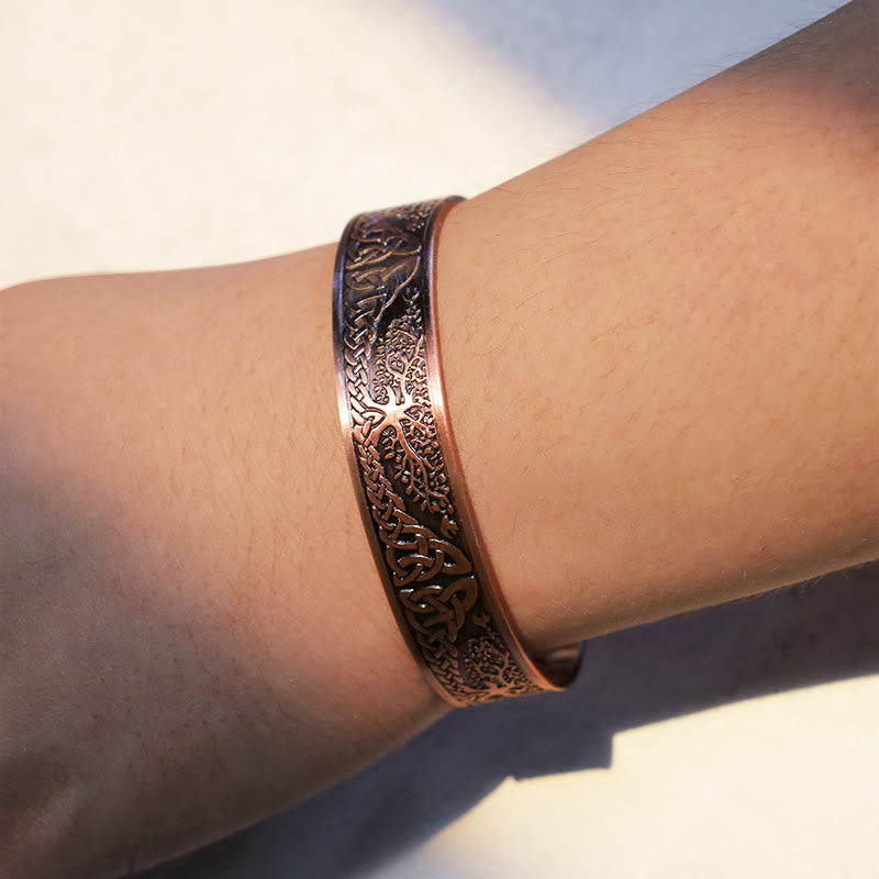 Copper tree of life cuff bracelet on wrist displaying relief-engraved Yggdrasil branches roots and Celtic endless knot patterns with antiqued patina finish