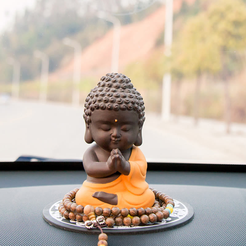 Small Buddha Purple Clay Decoration – yellow-robe prayer pose on dashboard with mala, suburban bokeh, spiritual travel compan