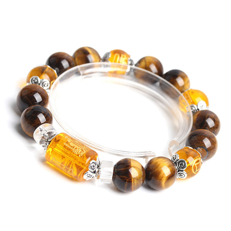 Overhead view of tiger eye stretch bracelet with carved amber focal bead, silver floral motif spacers and clear crystal accent beads on white background