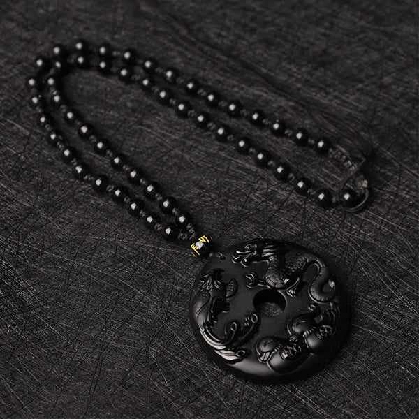 Black Obsidian Dragon Phoenix Pendant - Dragon-phoenix relief carving on polished obsidian disc on dark fabric, Protection