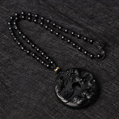 Black Obsidian Dragon Phoenix Pendant - Dragon-phoenix relief carving on polished obsidian disc on dark fabric, Protection
