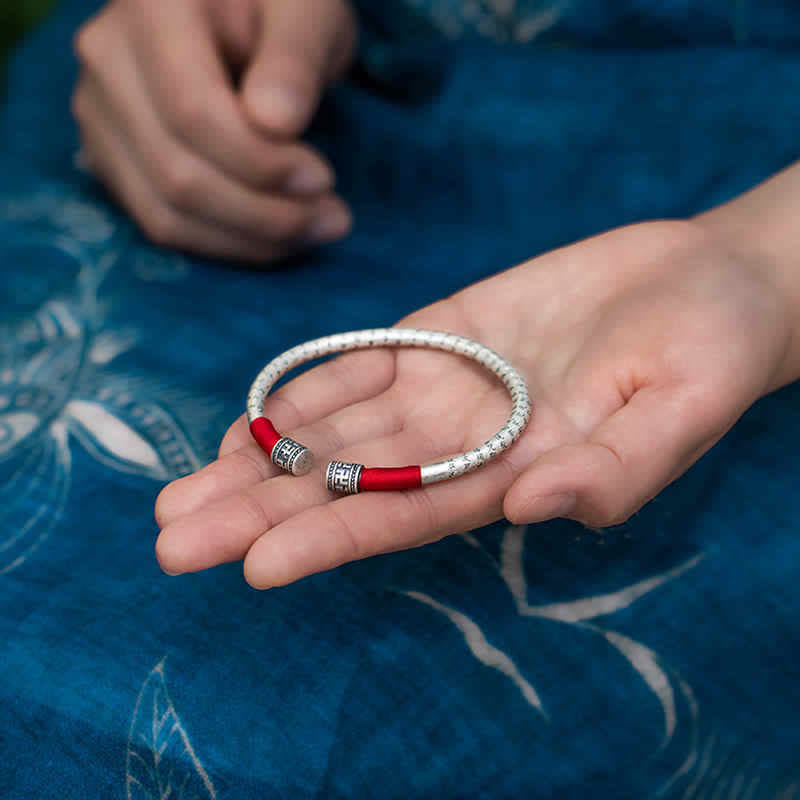 Tibetan Red String Bracelet – silver bangle held in palm against indigo textile, red cord detail