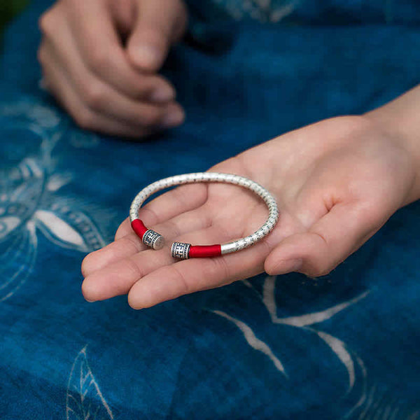 Tibetan Red String Bracelet – silver bangle held in palm against indigo textile, red cord detail