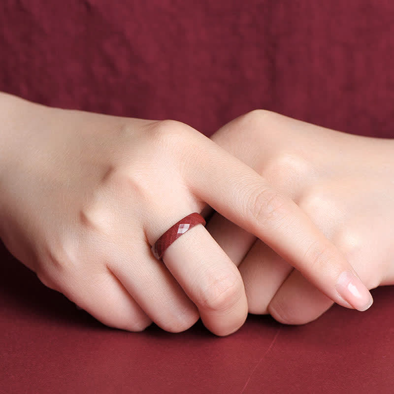 Cinnabar Om Mani Padme Hum Blessing Ring – faceted burgundy cinnabar ring on clasped hands, diamond-cut sparkle, monochrome styling