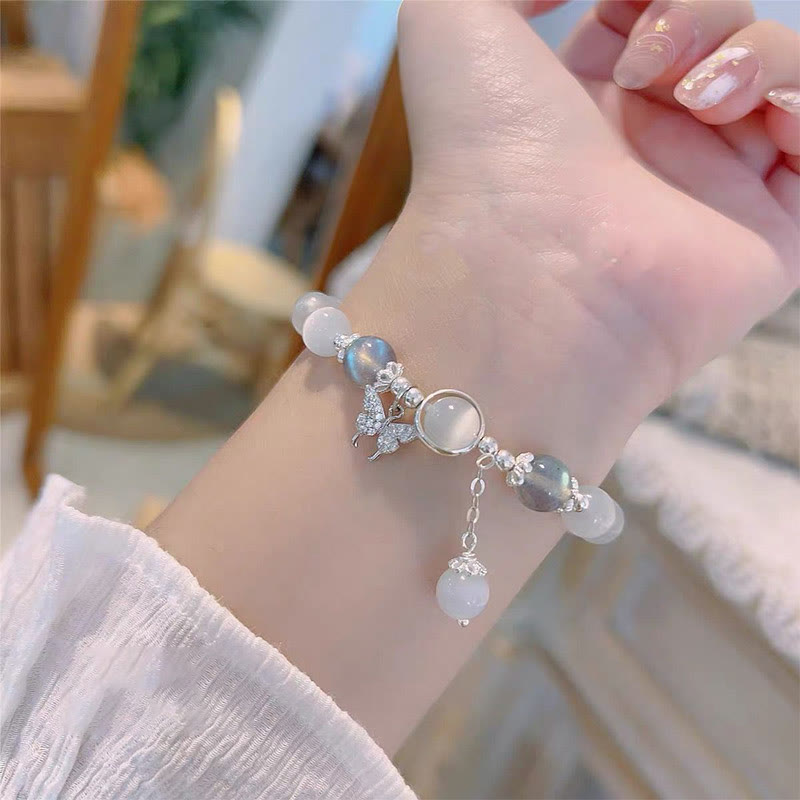 Cat's Eye Moonstone Butterfly Bracelet – White cat's eye beads with crystal butterfly charm and iridescent accents worn on wrist with white ruffled sleeve, lifestyle