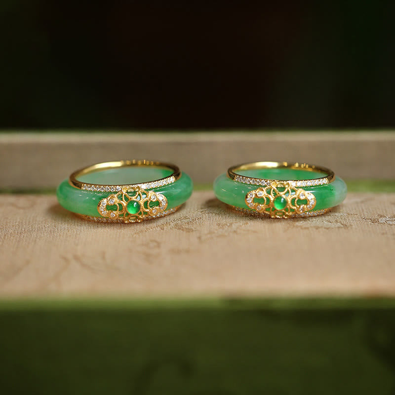 18K Gold Green Chalcedony Strength Ring – Two apple-green jade bangles with gold filigree diamond mounts and emerald cabochons on beige fabric, low front angle