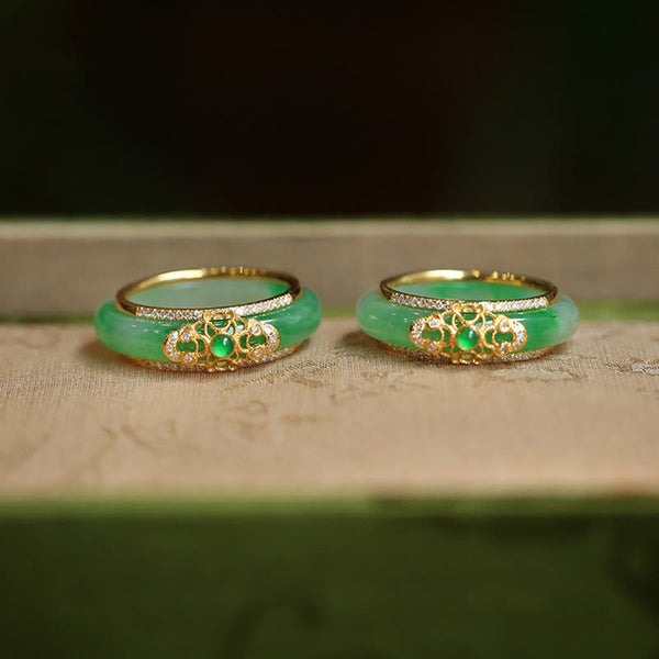18K Gold Green Chalcedony Strength Ring – Two apple-green jade bangles with gold filigree diamond mounts and emerald cabochons on beige fabric, low front angle