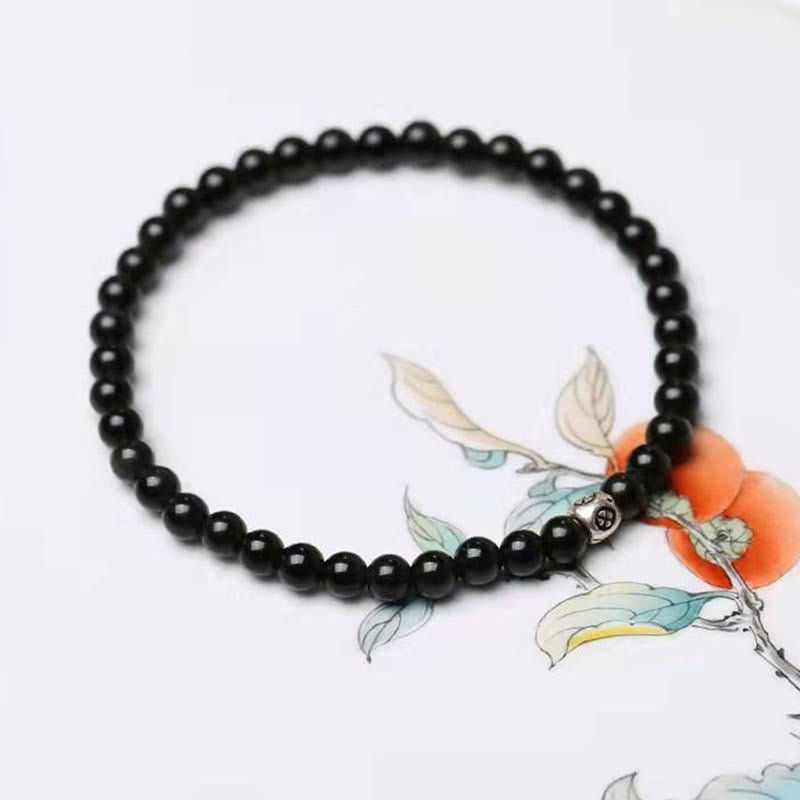Black Obsidian Smoky Quartz Bracelet – Polished black beads with silver-toned metal accent bead, white background with persimmon branch watercolor illustration, overhead flat lay