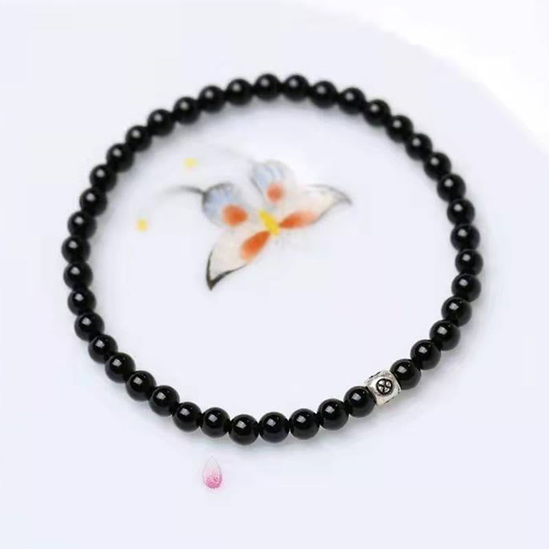Black Obsidian Smoky Quartz Bracelet – Black obsidian beads with silver patterned accent bead on white surface with floral watercolor painting, direct overhead view