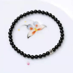 Black Obsidian Smoky Quartz Bracelet – Black obsidian beads with silver patterned accent bead on white surface with floral watercolor painting, direct overhead view