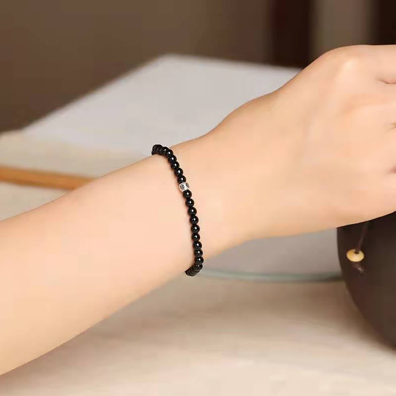 Black Obsidian Smoky Quartz Bracelet – Black obsidian beads with silver accent bead worn on wrist, neutral beige blurred background, side profile lifestyle shot