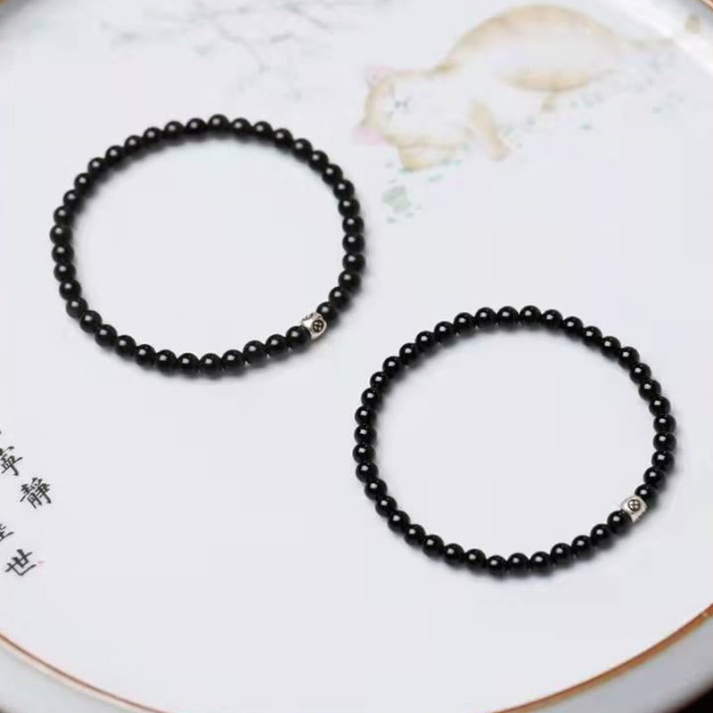 Black Obsidian Smoky Quartz Bracelet – Two identical black bead bracelets with silver accent beads on white ceramic plate with floral motifs and Chinese calligraphy, flat lay