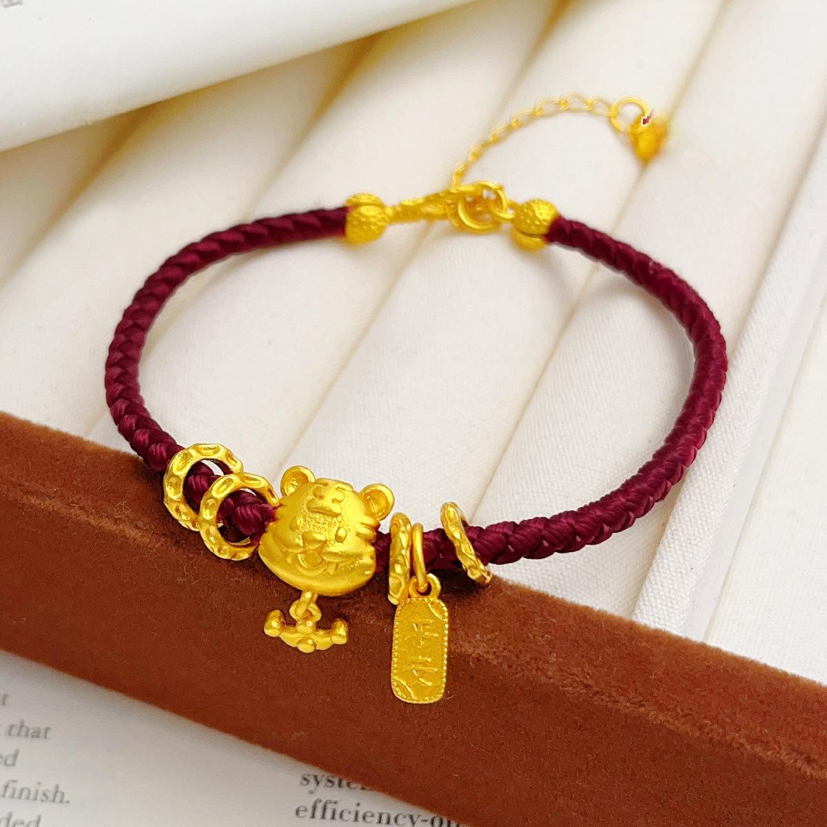 Ben Ming Nian Bracelet – gold tiger charm and engraved tag, maroon cord on white fabric, elegant