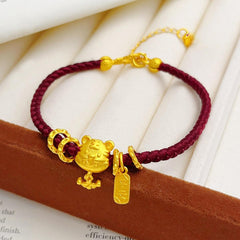 Ben Ming Nian Bracelet – gold tiger charm and engraved tag, maroon cord on white fabric, elegant