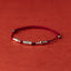 Koi Red String Bracelet – burgundy cord bracelet with silver fish bead and round beads on red surface, fortune jewelry
