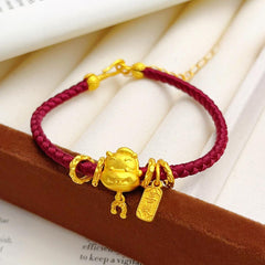 Ben Ming Nian Bracelet – gold ox charm on burgundy braided cord with peace tag, book background