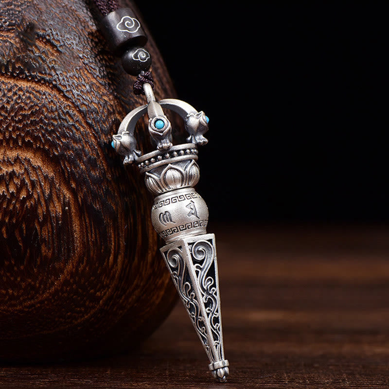 Tibetan Dorje Vajra Rotatable Pendant – Antiqued silver with turquoise inlays, lotus motifs and Sanskrit engravings on dark cord, dark wood vessel backdrop