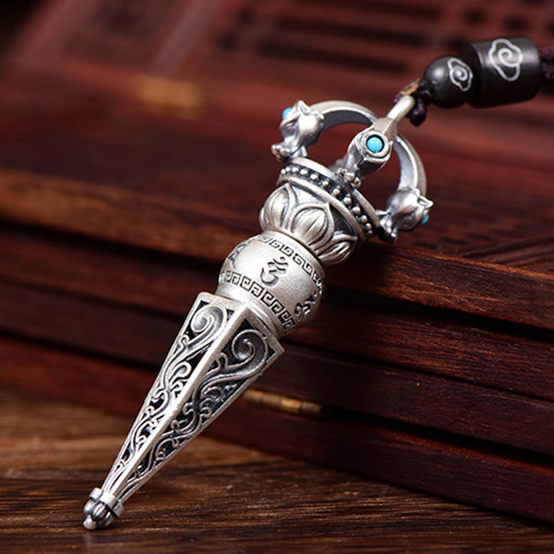 Tibetan Dorje Vajra Rotatable Pendant – Silver vajra with filigree scrollwork and turquoise stones on dark cord with cloud-pattern beads, dark wood slatted background