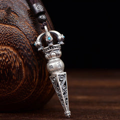Tibetan Dorje Vajra Rotatable Pendant – Antiqued silver with turquoise inlays, lotus motifs and Sanskrit engravings on dark cord, dark wood vessel backdrop