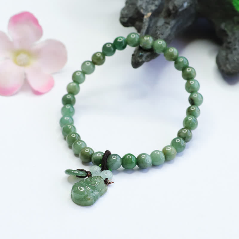 Polished cyan jade beaded bracelet with carved Laughing Buddha pendant and pale accent beads on white surface with ceramic bowl and pink floral prop