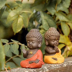 Small Buddha Purple Clay Decoration – two robe-color variants on weathered wood with green foliage, Serenity and Protection