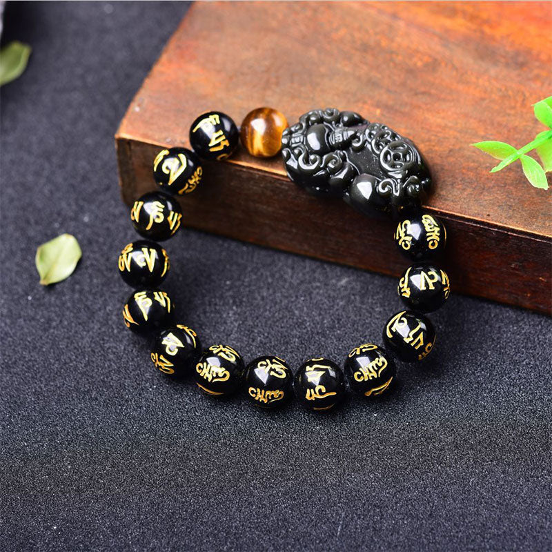 Obsidian PiXiu Rainbow Obsidian Wealth Bracelet – Black obsidian PiXiu bracelet on wood block with green leaves