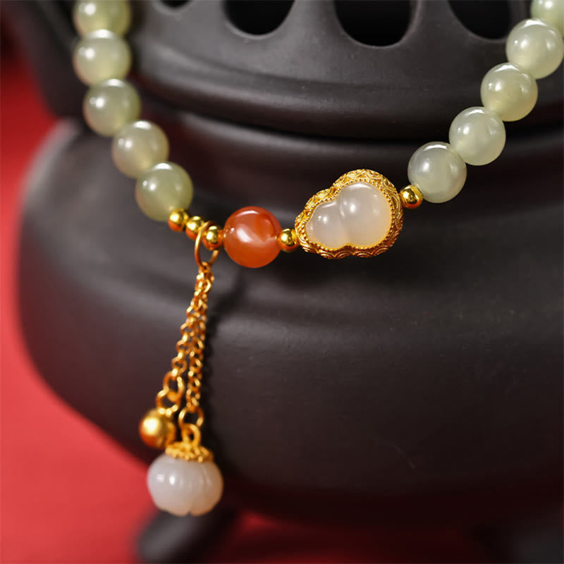 Gourd Lotus Bracelet gold filigree centerpiece with jade beads on black incense burner, red backdrop, artisanal