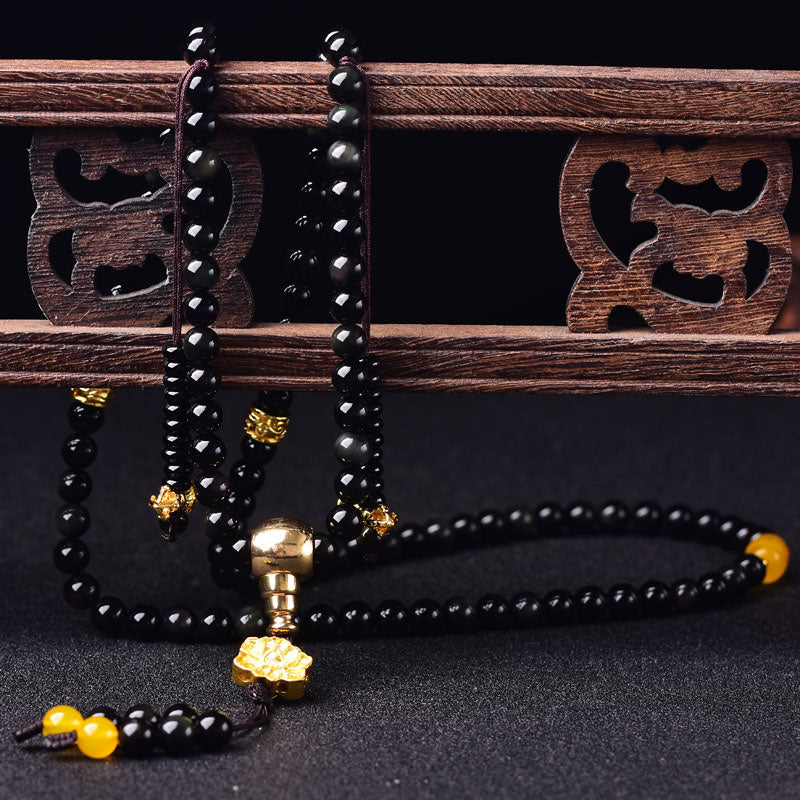 Black Obsidian Lotus Mala Bracelet - Hung over carved wooden lattice on black, gold lotus charm, obsidian