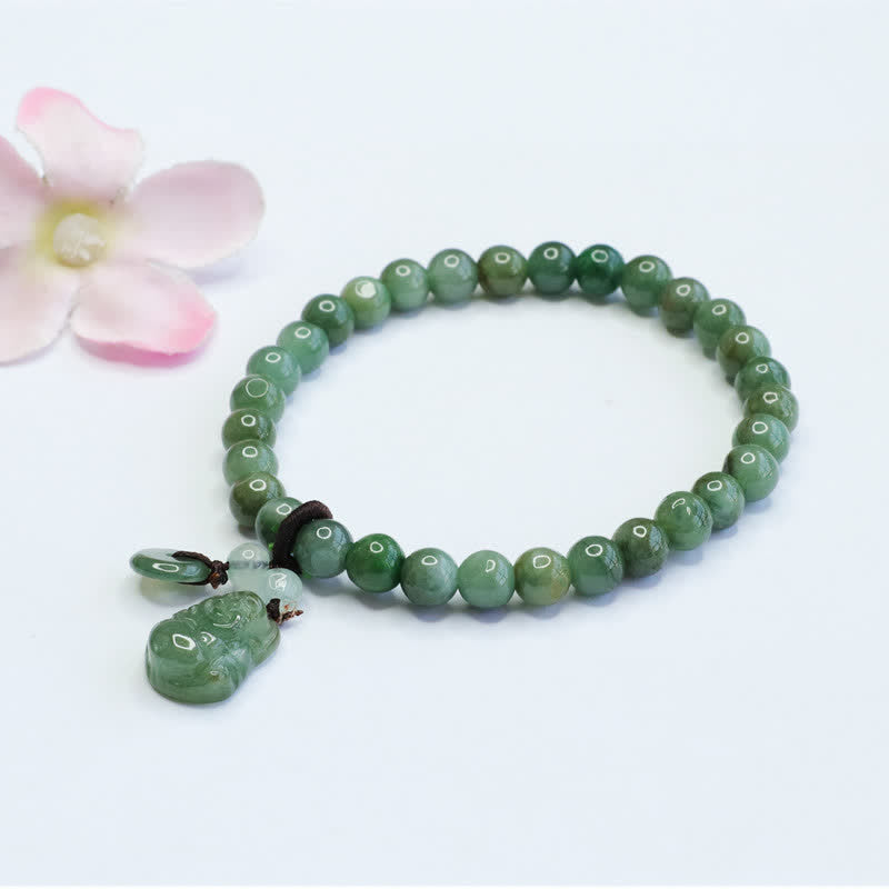Green jade beaded stretch bracelet with carved jade Pixiu charm and small disc pendant, pale translucent accent beads on white background with pink flower prop