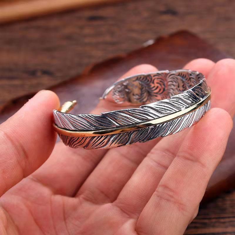 Feather-shaped sterling silver cuff bracelet held in hand, two-tone silver and gold with etched barb details and engraved interior patterns