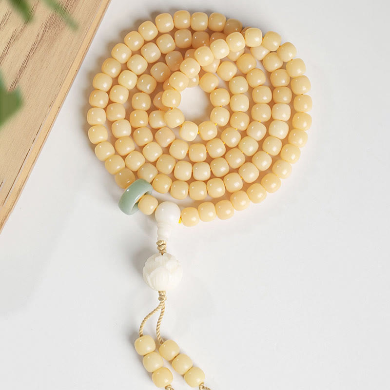 Bodhi Seed Lotus Dzi Bracelet - Overhead coiled mala on white surface with wood and green foliage, bodhi seed