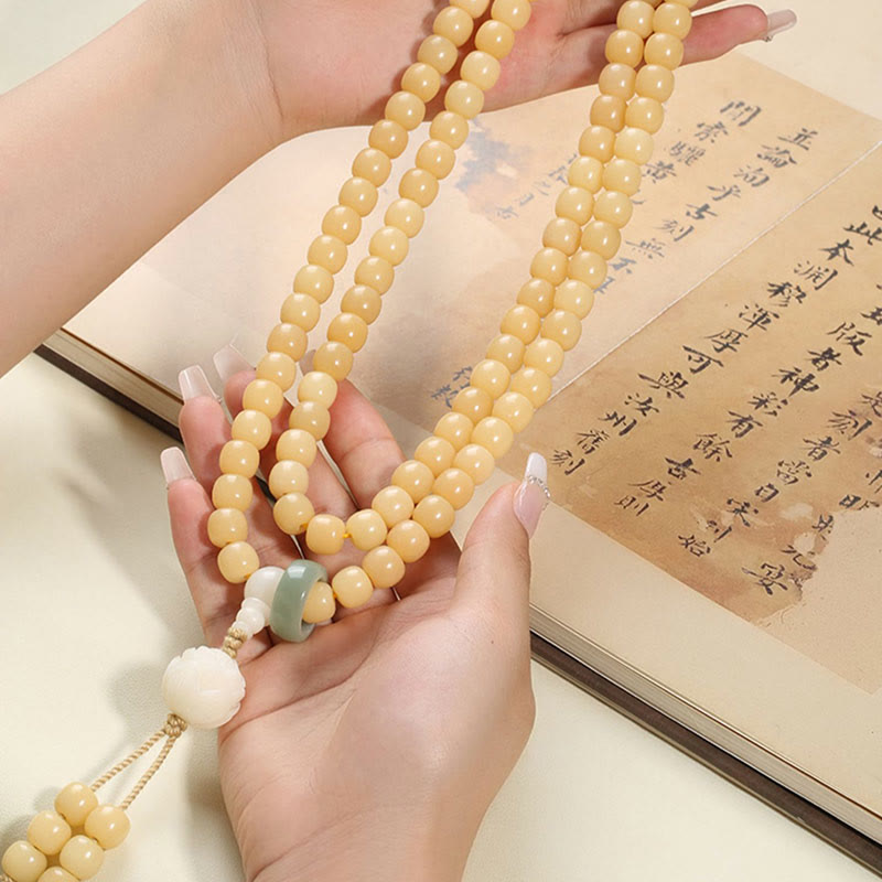 Bodhi Seed Lotus Dzi Bracelet - Mala held above open calligraphy book on cream surface, prayer bead necklace