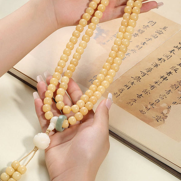 Bodhi Seed Lotus Dzi Bracelet - Mala held above open calligraphy book on cream surface, prayer bead necklace