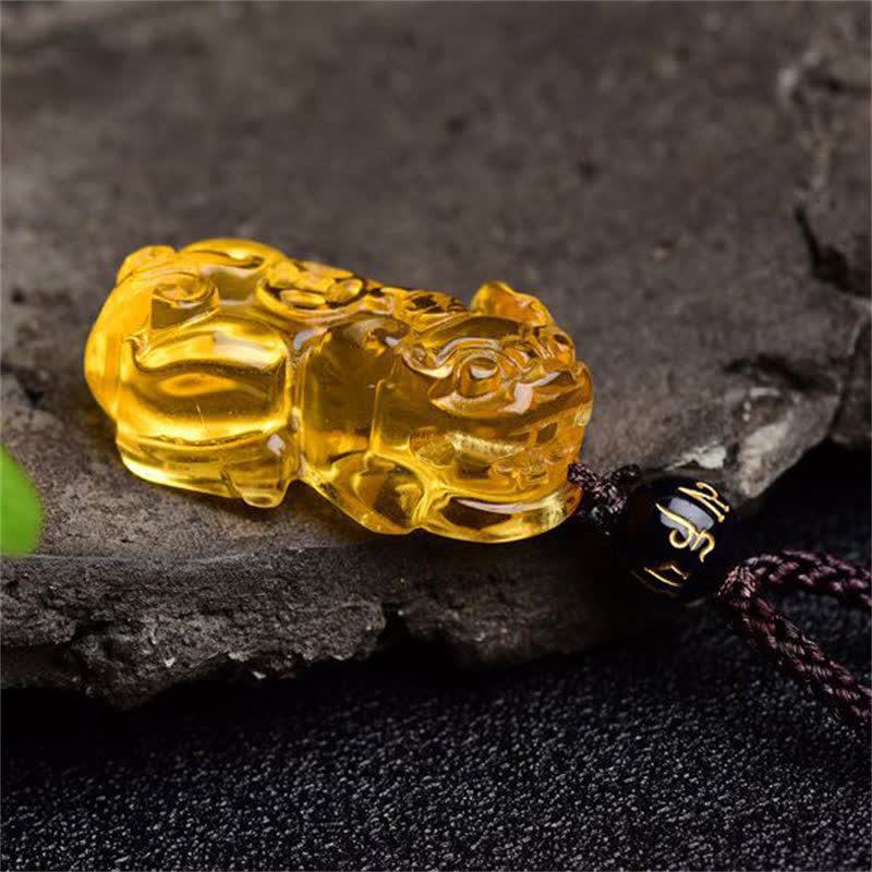 Citrine PiXiu Necklace Pendant – Yellow citrine PiXiu lying on dark stone, side angle prosperity charm