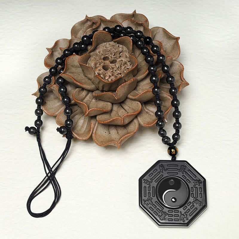 Black Obsidian Yin Yang Pendant Necklace - flat lay on ceramic lotus flower, black obsidian beaded chain with bagua pendant