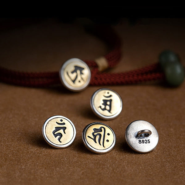 925 Silver Zodiac Natal Buddha charm collection flat lay, five interchangeable circular two-tone medallion pendants with Sanskrit seed syllables, S925 sterling silver hallmark, olive green jade bead, burgundy cord detail