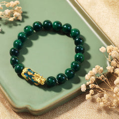 PiXiu Jade Bracelet – Dark green jade beads with gold PiXiu on green tray with dried flowers