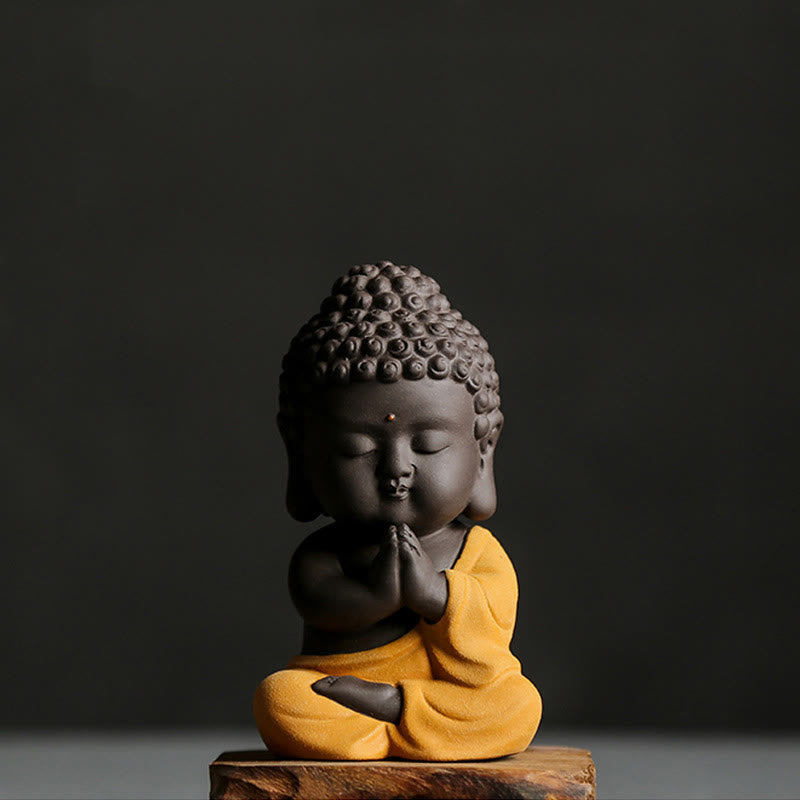 Small Buddha Purple Clay Decoration – yellow-robe variant on wood base, anjali prayer pose, low angle dark gray backdrop, dev