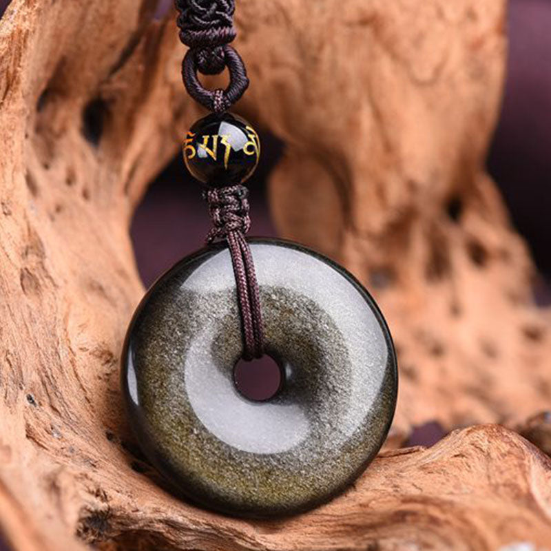 Golden silver sheen obsidian bi disc necklace showing chatoyant rainbow iridescence with Tibetan mantra bead on knotted dark cord on natural driftwood backdrop