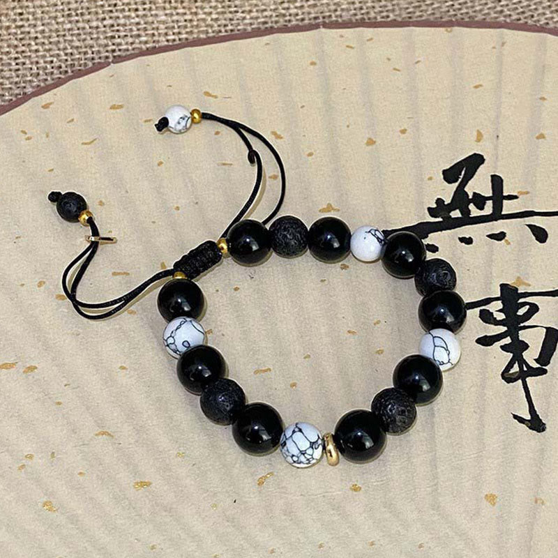 Black Obsidian Lava Rock Yin Yang Bracelet - flat lay on gold fleck paper with Chinese calligraphy fan, artisan style