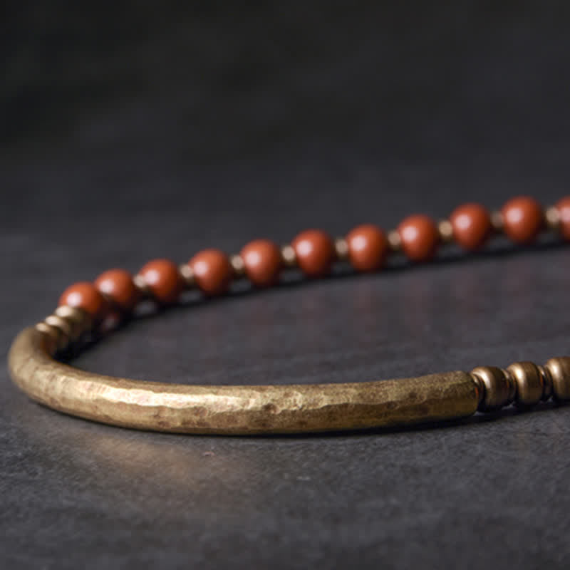 Close-up of red jasper bracelet showing hand-hammered antique brass curved bar with terracotta stone beads and bronze spacer beads, artisan boho jewelry detail