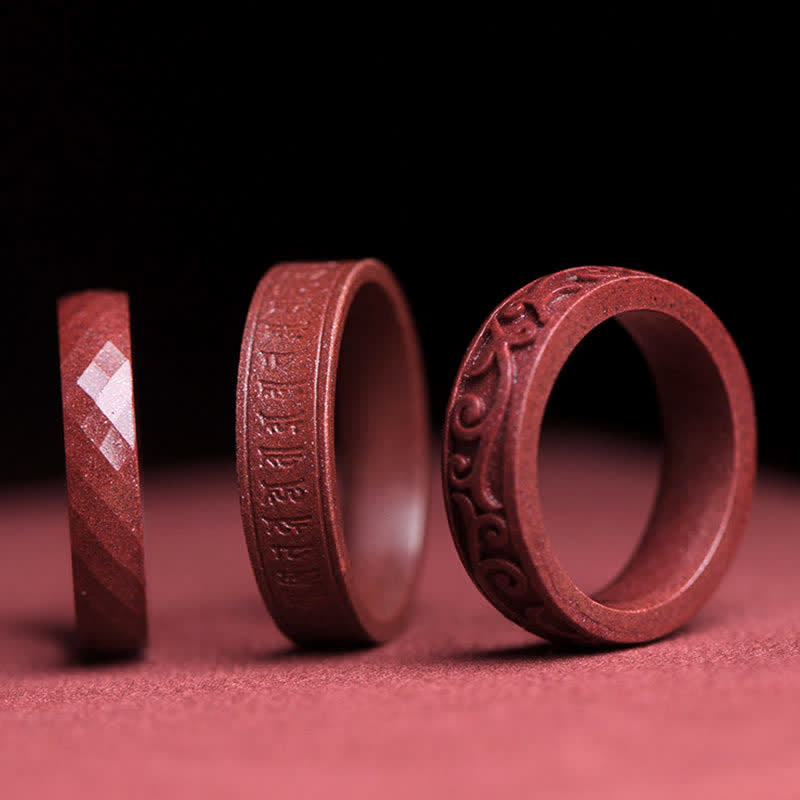 Cinnabar Om Mani Padme Hum Blessing Ring – three vermilion cinnabar rings with carved mantra, facets and cloud motifs, dark studio background