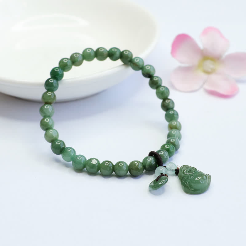 Cyan jade stretch bracelet with carved jade Pixiu wealth charm and disc pendant on white background with white ceramic dish and pink flower accent