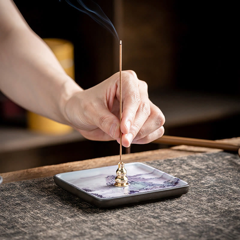 Mountain Lake Incense Holder – Hand placing incense stick in brass gourd holder on painted ceramic plate